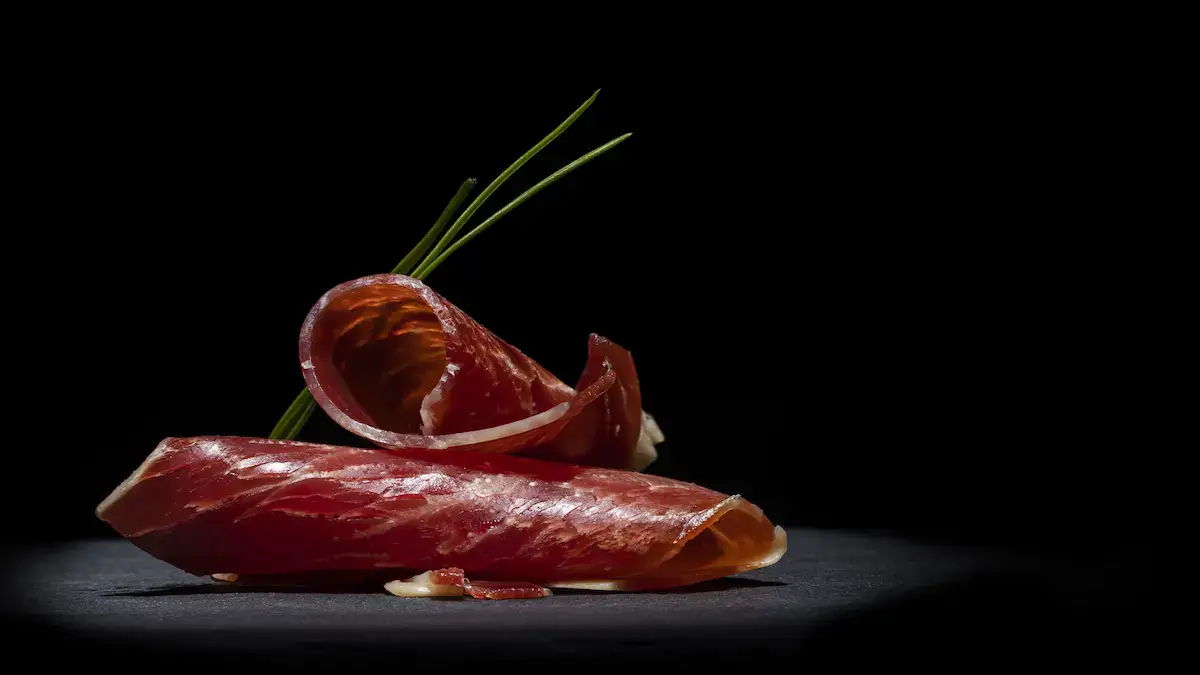 Lonchas de jamón ibérico de bellota gourmet con grasa translúcida en fondo oscuro