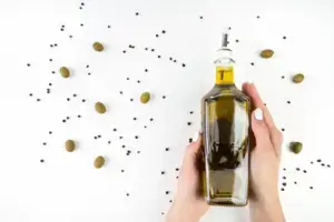 Manos sosteniendo una botella de aceite de oliva virgen extra con aceitunas sobre fondo claro